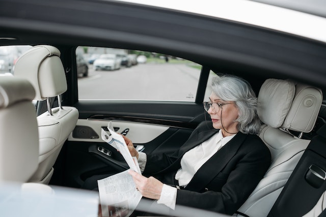 Elegant woman reading a newspaper in the backseat of a luxury vehicle, representing a comfortable taxi from Liverpool to Manchester Airport